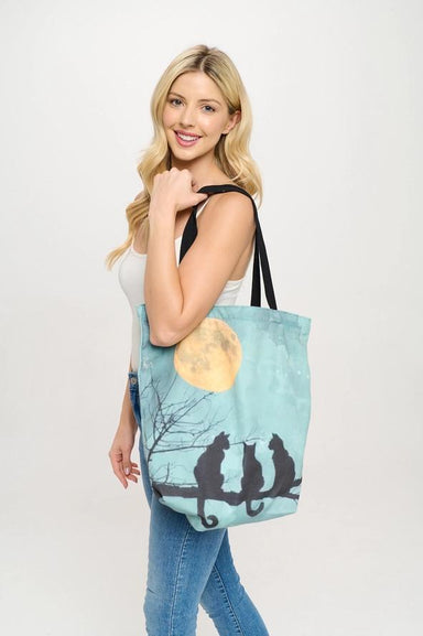 Woman holding a tote bag with a design of three cats on a branch under a moon.