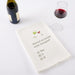 Wine-themed kitchen towel with humorous question and drink icons on a white surface with wine bottle and glass.
