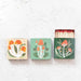 Three matchboxes with mushroom designs on a textured white surface