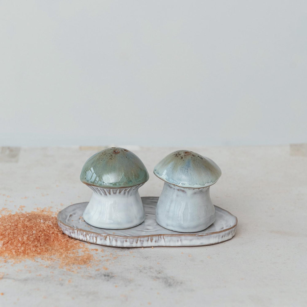 Two ceramic mushroom-shaped salt and pepper shakers on a matching tray with a light background.
