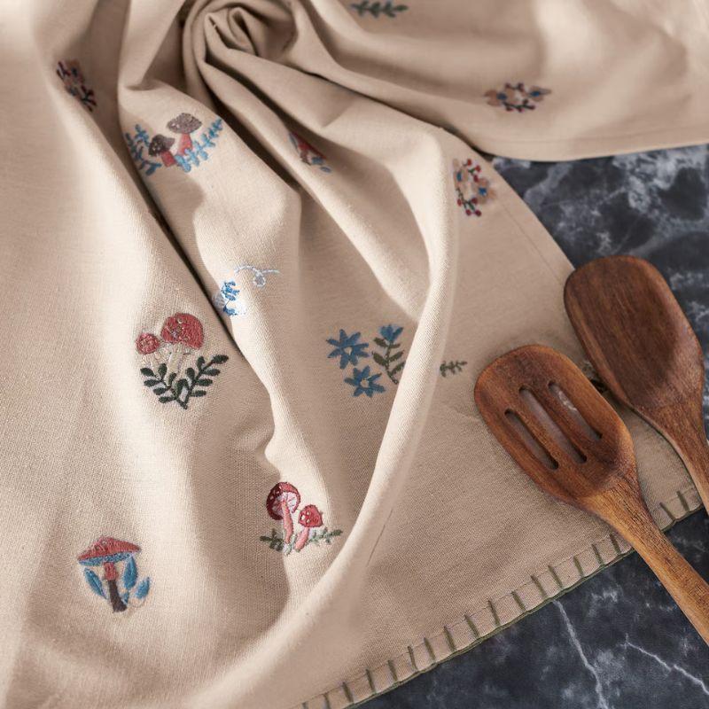 Beige towel with floral embroidery on a marble surface with wooden utensils.