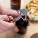 Person using a bottle opener on a beer bottle with food in the background
