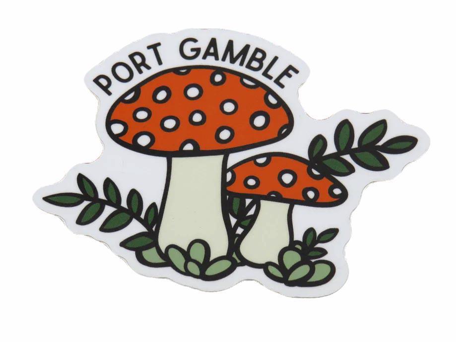 A die-cut sticker featuring two red and white spotted mushrooms with green leaves and the text 'PORT GAMBLE' arched above them, shown on a plain white background.