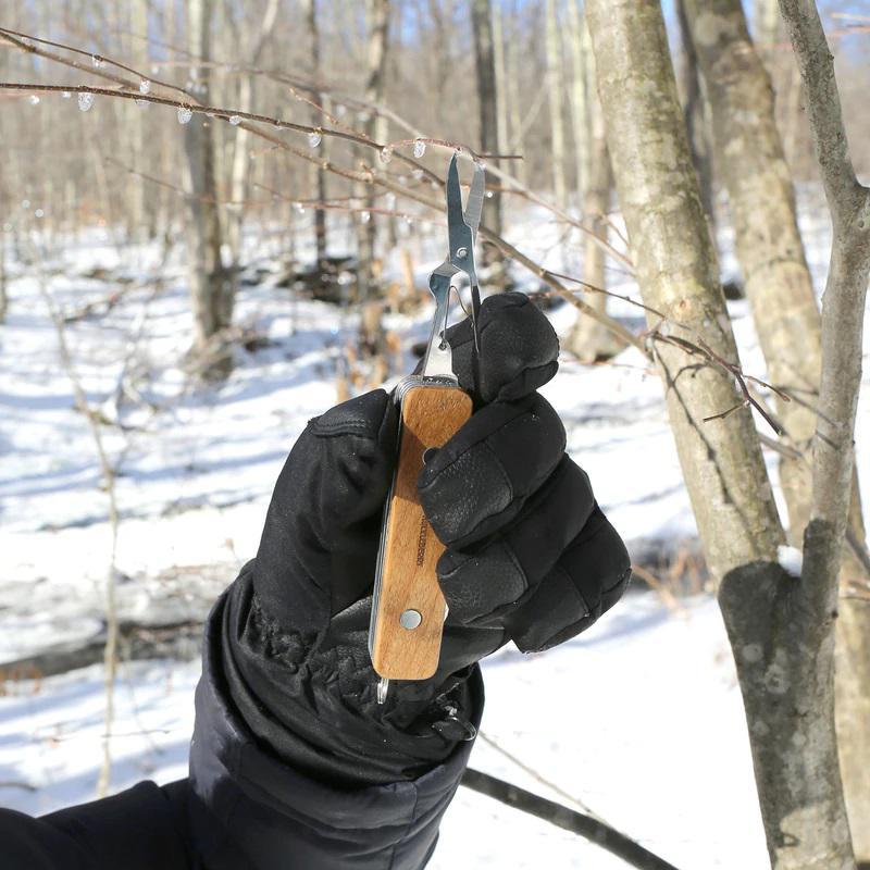 Person holding a pair of pliers with wooden handle in a snowy forest