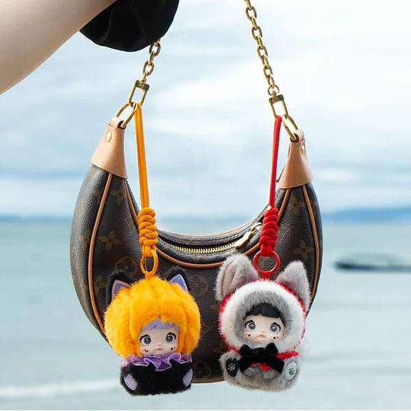 Two plush keychains on a handbag with a blurred ocean background