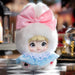 Small doll with white fur coat, pink bow, and blue dress on a checkered floor.