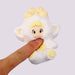 Plush toy resembling a character with blonde hair and a white outfit held by a hand against a light gray background