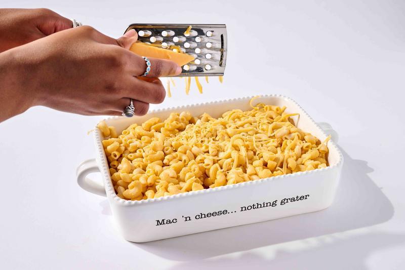 Person grating cheese over a dish of macaroni and cheese with a grater.