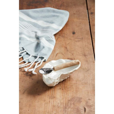 Light blue towel with white stripes draped over a wooden surface, next to a shell with a spoon inside.