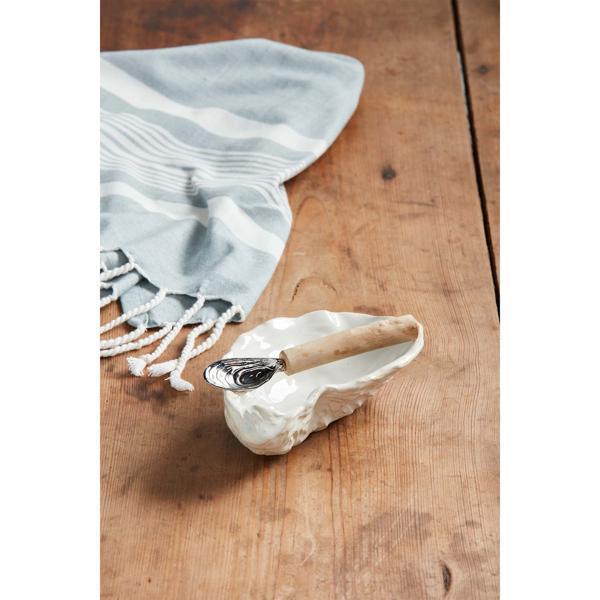 Light blue towel with white stripes draped over a wooden surface, next to a shell with a spoon inside.