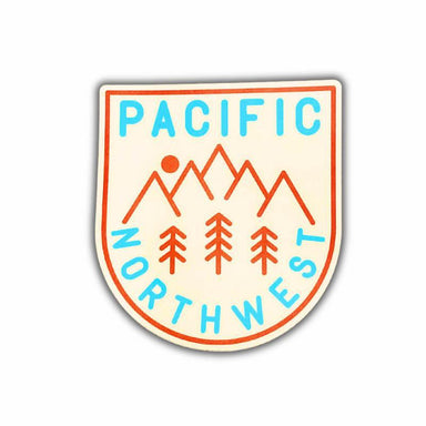 A shield-shaped sticker featuring the words 'PACIFIC NORTHWEST' in light blue, with orange mountain peaks, trees, and a sun on a cream background, shown on a white background.