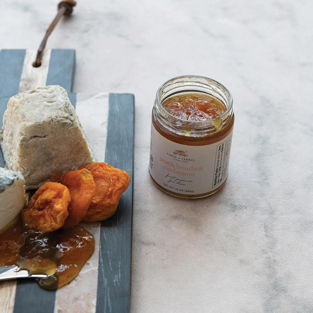 Jar of apricot preserves on a marble surface with cheese and dried apricots.