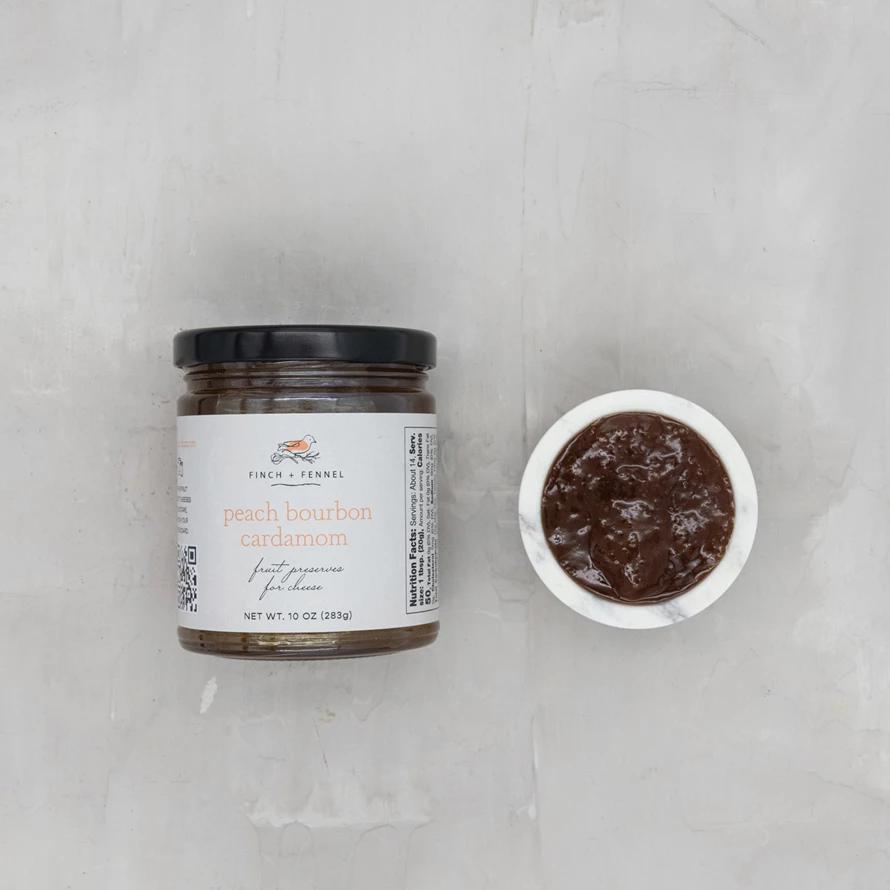 Jar of peach bourbon caramel sauce with a small bowl of the sauce on a light gray background