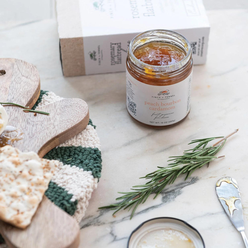 Jar of peach lemon honey on a marble surface with crackers and rosemary.