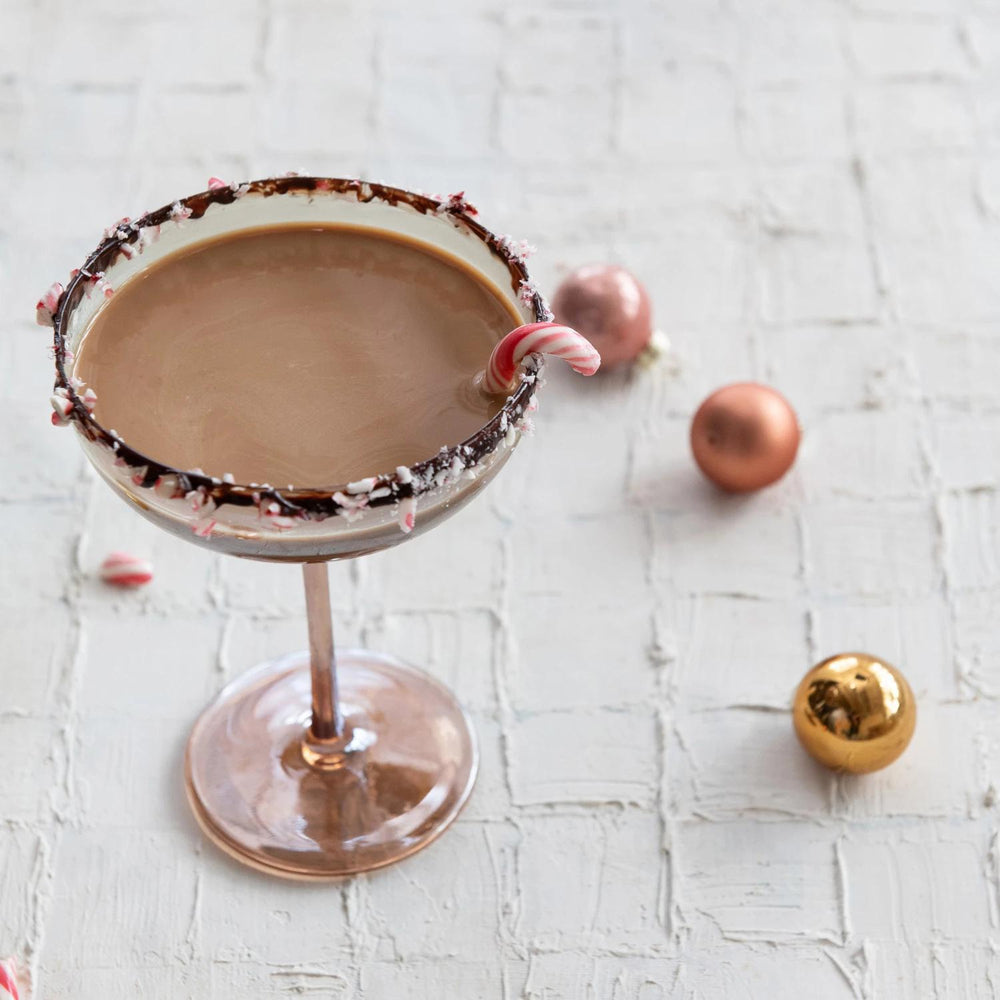 Chocolate cocktail in a martini glass with candy cane on a textured white surface