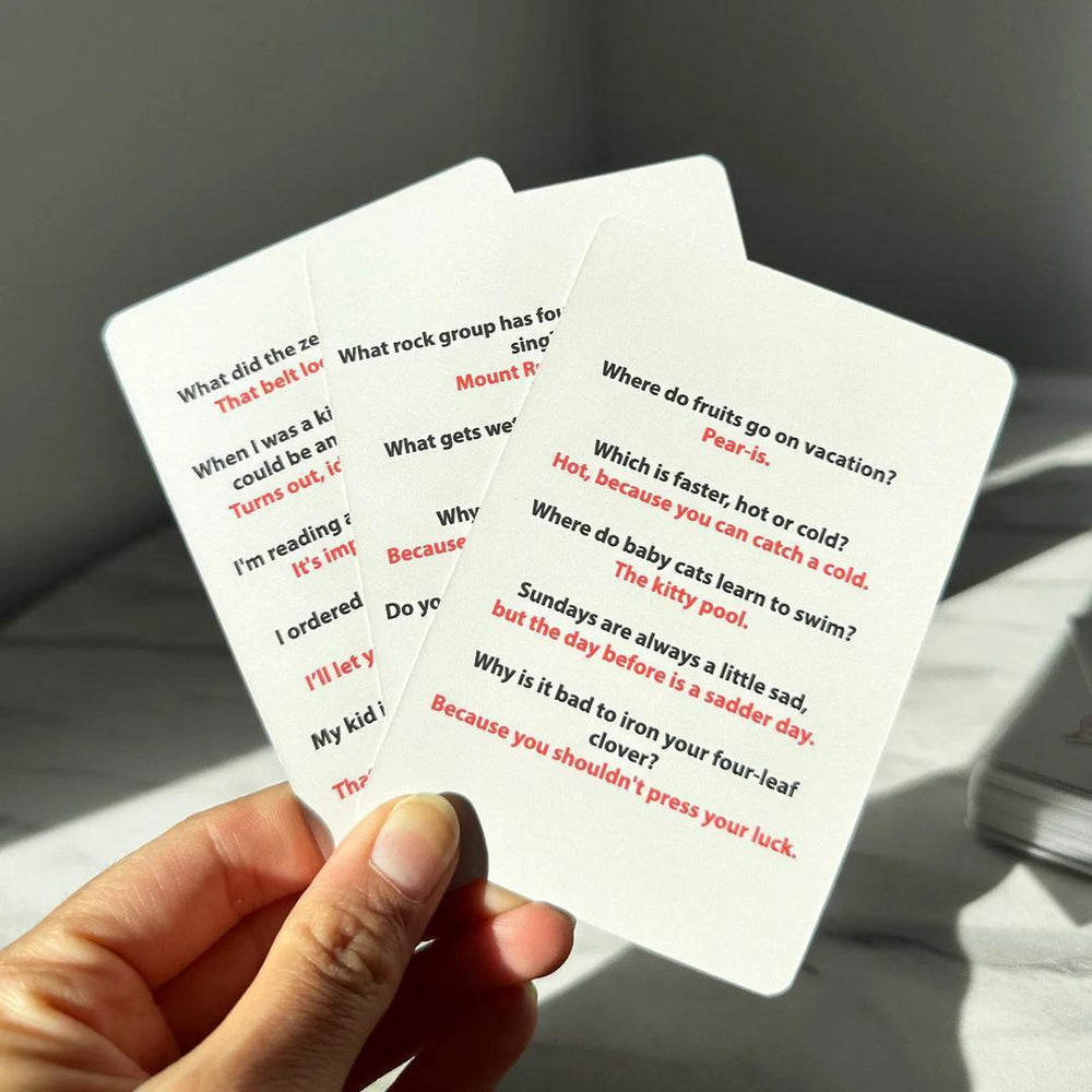 Hand holding three playing cards with humorous text, on a light surface.