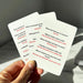 Hand holding three playing cards with humorous text, on a light surface.