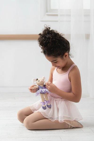 Young girl in a ballet outfit playing with a teddy bear on a white floor.