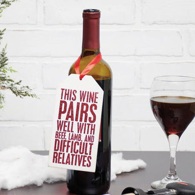 Wine bottle with a humorous label next to a glass of wine on a white brick wall background