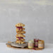 Stack of scones with jam and cream on a wooden board with jars of jam and cream against a gray background.