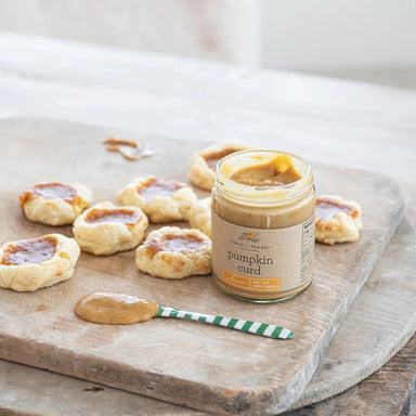 Jar of pumpkin curd on a wooden board with biscuits and a spoon