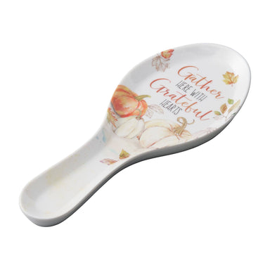 A white ceramic spoon rest with a fall harvest design, featuring watercolor pumpkins, leaves, and the phrase 'Gather Here With Grateful Hearts' in orange and brown lettering.