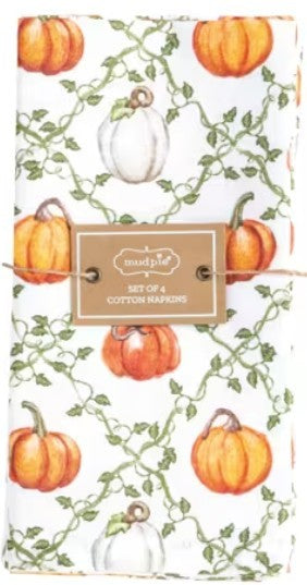 A folded white cotton napkin with an all-over autumn print of orange and white pumpkins, green vines, and leaves, secured with a twine strap and a central paper label that reads 'mudpie' and 'Set of 4 Cotton Napkins'.