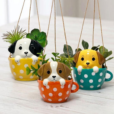 Three hanging planters shaped like dogs in polka dot mugs on a wooden surface.