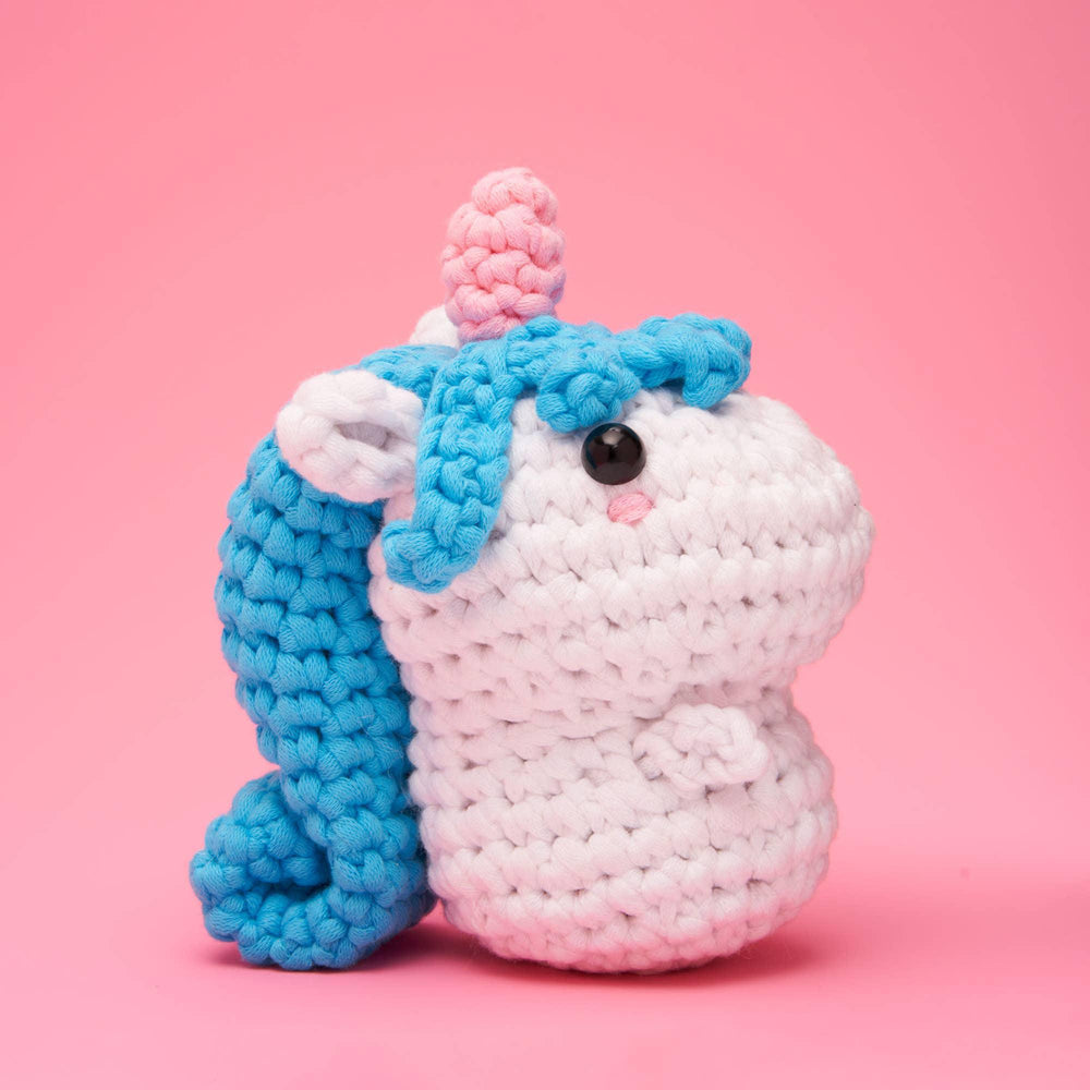 Crocheted unicorn toy with blue mane and tail on a pink background