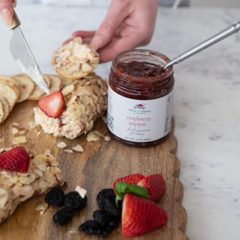 Wooden board with a dessert, jar of raspberry pepper jam, and fresh berries on a marble surface.