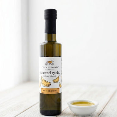 Bottle of roasted garlic infused olive oil with a small bowl of oil on a white background