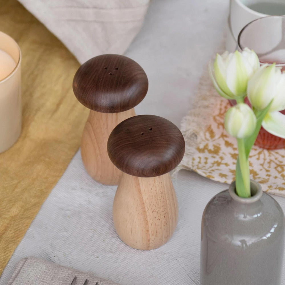 Wooden mushroom-shaped salt and pepper shakers on a table with a vase and flowers.