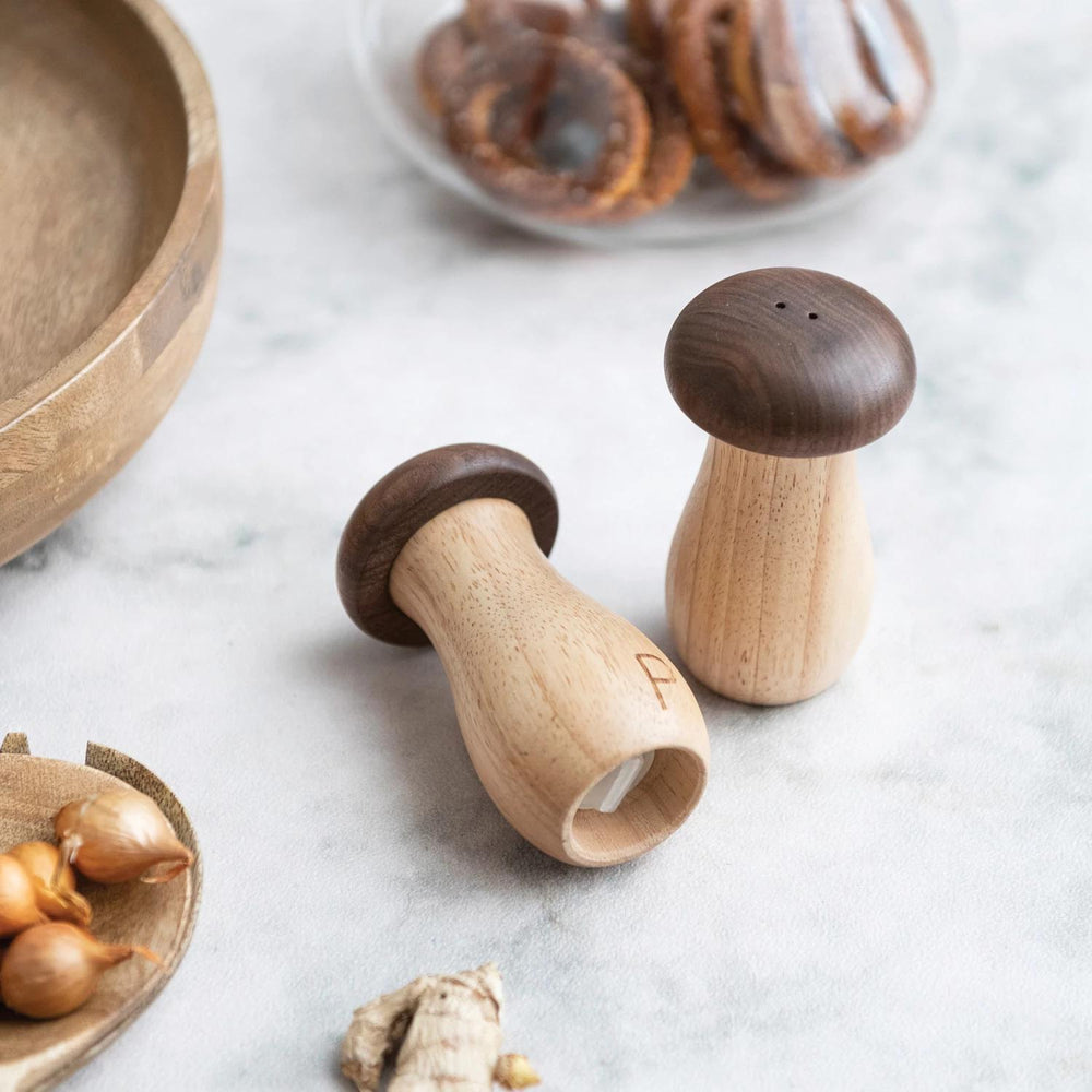 Wooden salt and pepper shakers on a marble surface with a plate of bagels in the background.