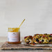 Jar of aronia pepper jam with a loaf of bread on a wooden board against a light background