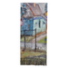 A rectangular woven textile with fringe along the bottom edge, featuring an artistic depiction of a house and fence in soft blue, green, brown, and gray tones, shown against a light gray background.