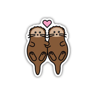 A die-cut sticker featuring two cute cartoon brown otters facing each other with a small pink heart above them, shown on a plain white background.