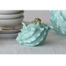 Turquoise ceramic shell-shaped container with a small shell on top, placed on a light surface.