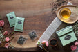 Tea packaging and loose tea on a wooden surface with flowers and a teacup.