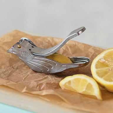 Metallic bird-shaped lemon squeezer on brown paper with sliced lemons.