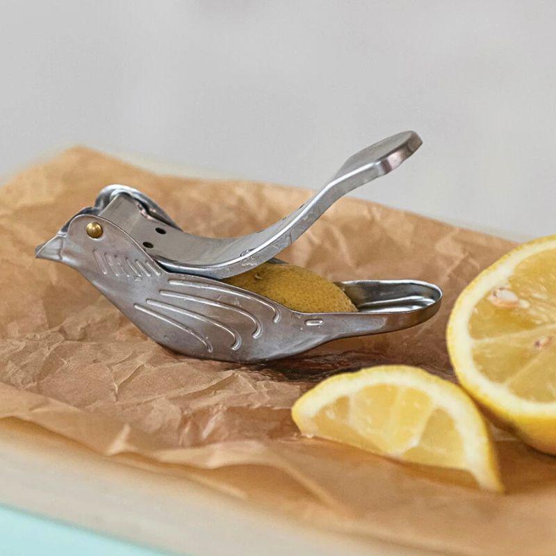 Metallic bird-shaped lemon squeezer on brown paper with sliced lemons.
