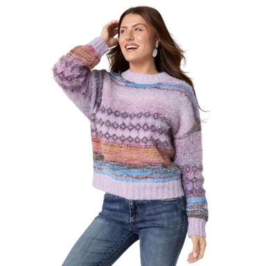 A woman wearing a fuzzy knit crewneck sweater with a multicolor Fair Isle pattern in shades of purple, pink, orange, and blue, paired with blue jeans, against a plain white background.