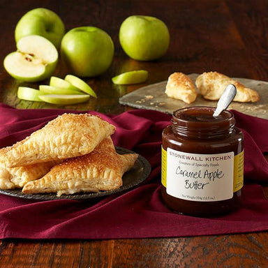 Jar of Stonewall Kitchen Caramel Apple Butter with apple turnovers and apples on a wooden table.