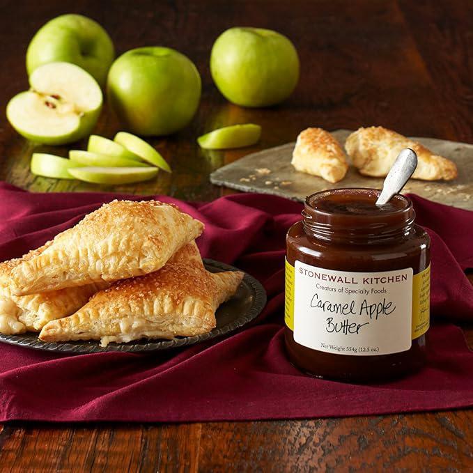 Jar of Stonewall Kitchen Caramel Apple Butter with apple turnovers and apples on a wooden table.