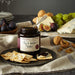 Stonewall Kitchen Fig & Walnut Butter jar on a plate with crackers and figs, surrounded by cheese and grapes.