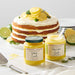 Lemon and lime curd jars with a layered cake on a light background