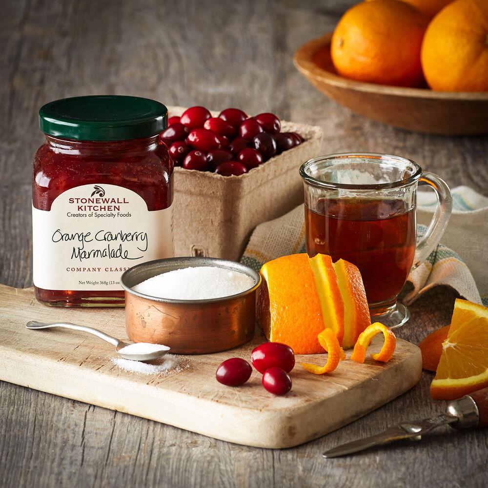 Stonewall Kitchen Orange Cranberry Marmalade jar with oranges, cranberries, and a mug of tea on a wooden board.