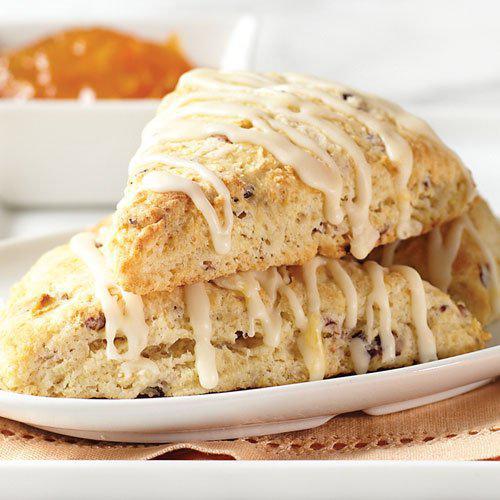 Two scones with a white drizzle on a white plate, with a blurred background.