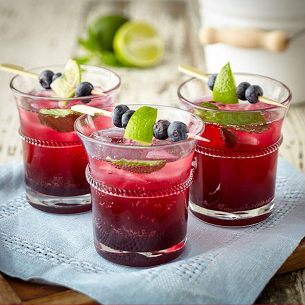 Three small glasses of red cocktails with lime wedges and blueberries on a light blue napkin.