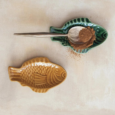 Fish-shaped ceramic container with a spoonful of brown powder on a beige background