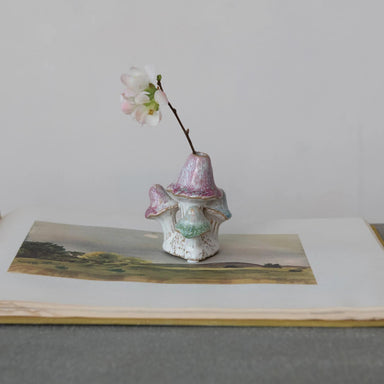 Small ceramic vase with a branch and flowers on a landscape print